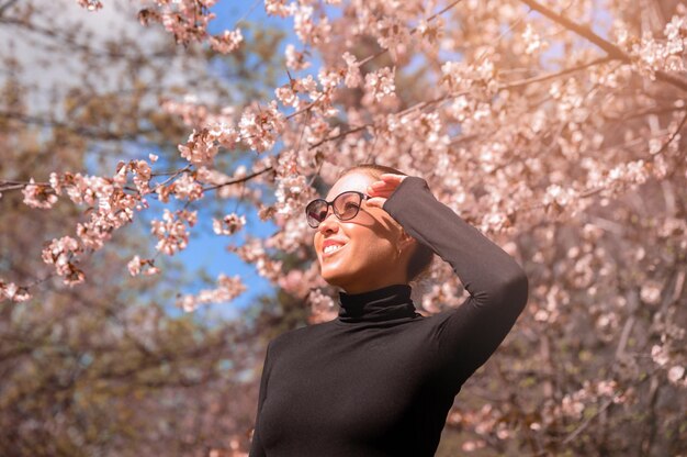 花の木のそばに立っているサングラスをかぶった若い女性の低角度の写真