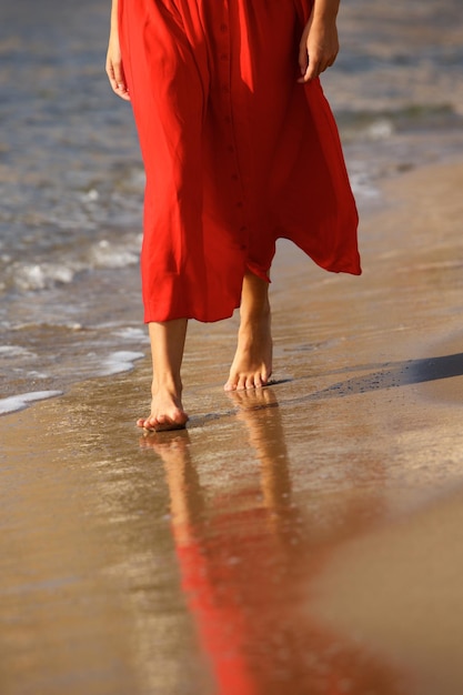 Low angle of woman walking barefoot on beach in red dress