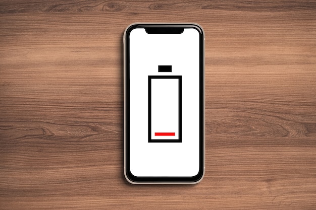 低バッテリーアイコンは、木製の背景にスマートフォンでモックアップします。
