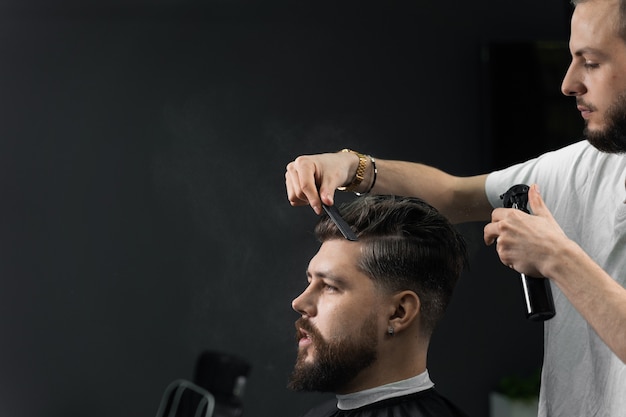 Low fade machine haircut for handsome bearded man in barbershop. Barber with dread locks making hairstyle with a smooth transition.