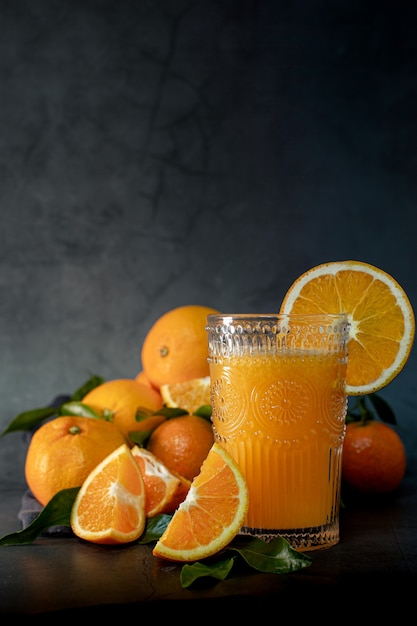 写真 絞る準備ができているオレンジのセットの横にある新鮮なオレンジジュースのグラスのローキーライト画像