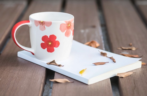 Low key photo of beautiful cup of coffee on white book on wooden table with dried leaves with dark tone and selection focus