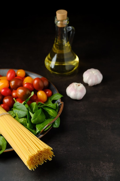 Low key photo of bunch of raw spaghetti with spinach, tomato, garlic and olive oil