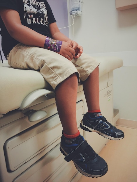 Photo low section of boy sitting on bed in clinic