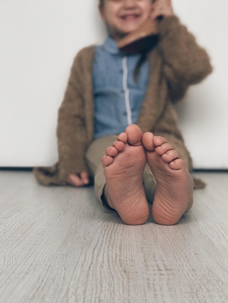 Foto sezione bassa di un ragazzo seduto sul pavimento contro il muro a casa