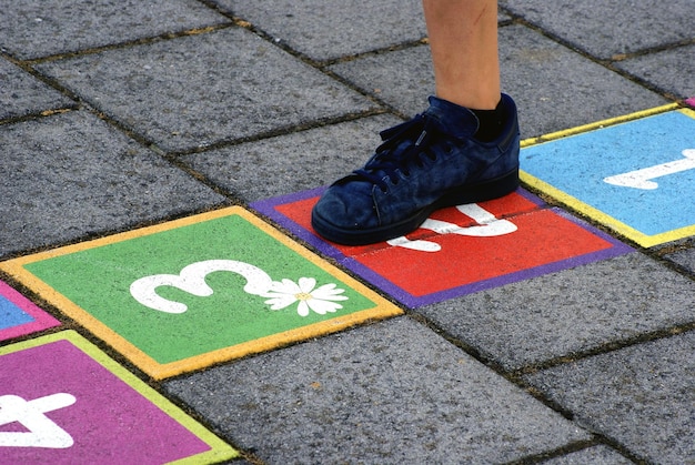 Foto sezione bassa di un bambino che gioca a hopscotch sul sentiero