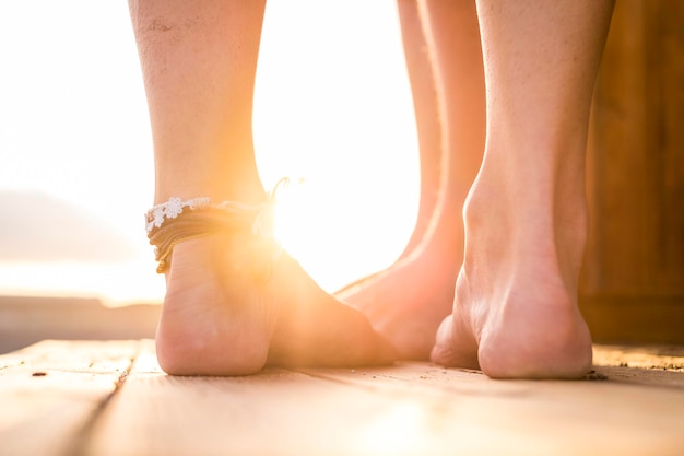 Low section of couple standing on floorboard at beach during sunset