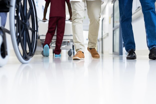 Photo low section of diverse male doctors and wheelchair in busy hospital corridor, copy space. hospital, medical and healthcare services.