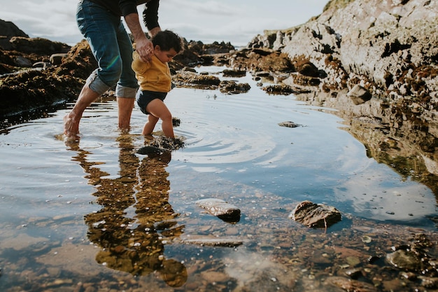 low section of father and daughter wading in puddle against sky