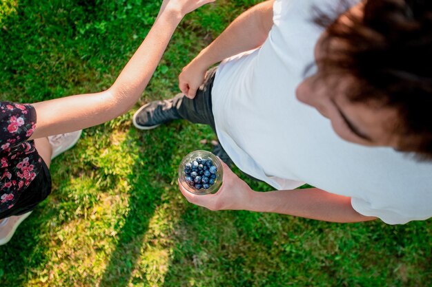 Photo low section of girl by brother with blueberries in glass standing on field