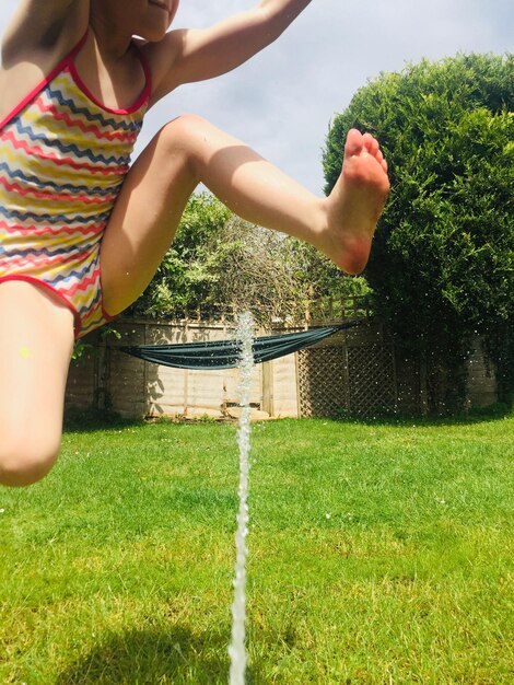 Foto sezione bassa di una ragazza che salta sull'acqua su un terreno erboso