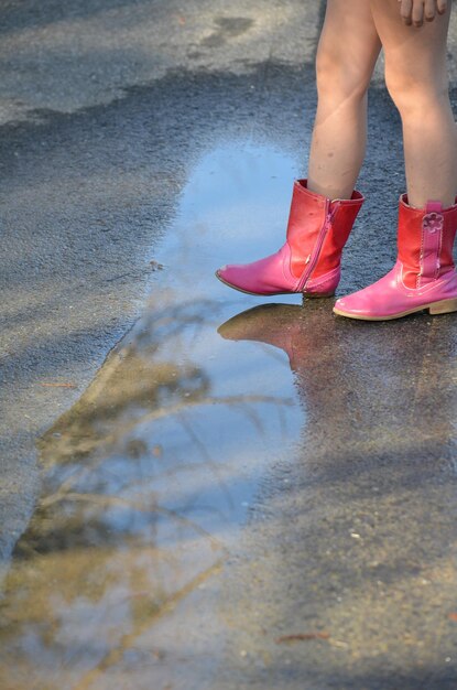 Photo low section of girl with pink boot standing on puddle