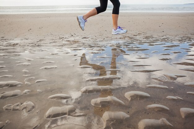 Low section of a healthy woman jogging on beach