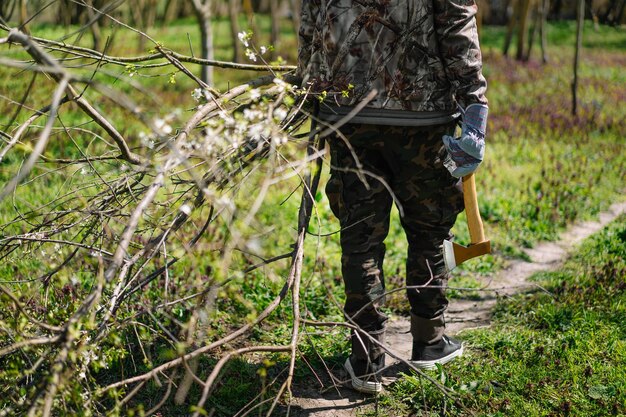 Foto sezione bassa di un uomo che porta rami tagliati e un'ascia nella foresta