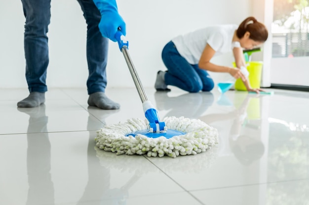 Low section of man cleaning floor with mop by woman at home