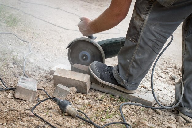 Low section of man cutting concrete brick with circular saw