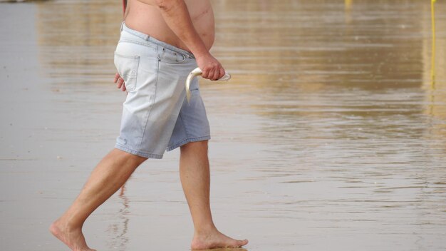 Photo low section of man holding fish while walking on beach