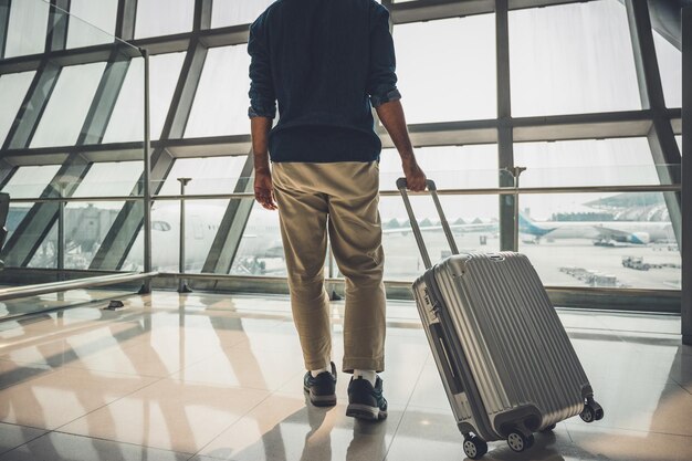 Low section of man holding suitcase walking on floor at airport