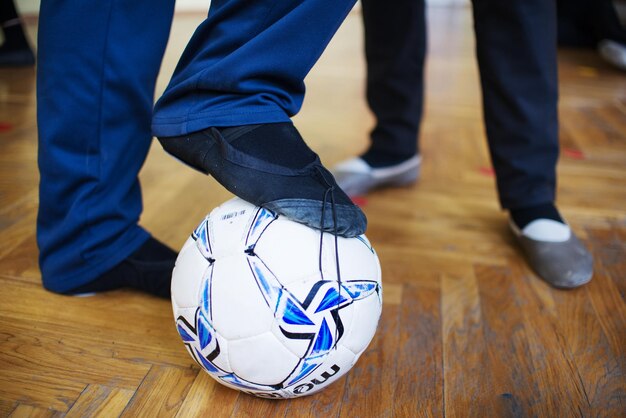 Photo low section of man leg with football while standing on wooden floor