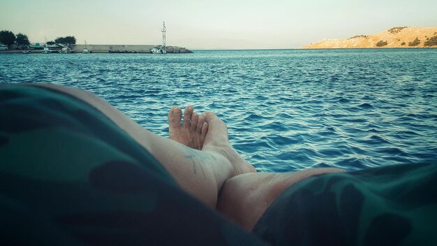 Low section of man resting by sea against clear sky