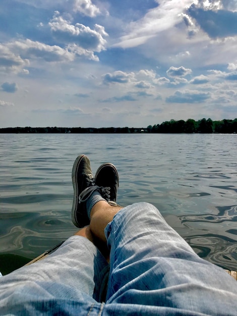 Photo low section of man sitting by lake against sky