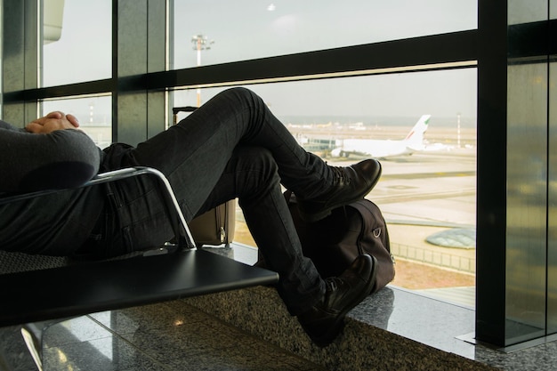 Photo low section of man sitting on chair by glass window at airport