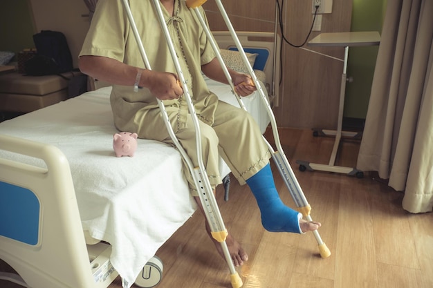 Photo low section of man sitting on hospital bed with crutches