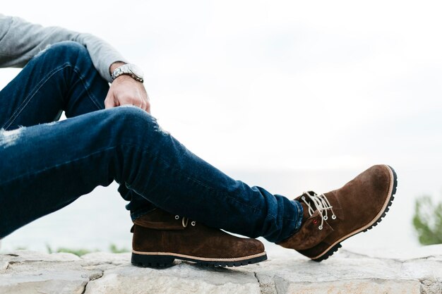 Low section of man sitting on retaining wall against sky