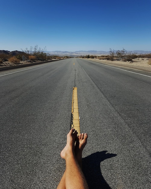 Foto sezione bassa di un uomo seduto sulla strada contro un cielo blu limpido