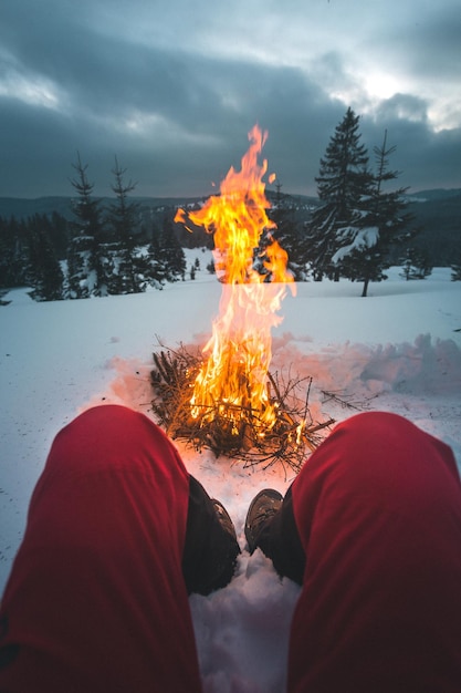 low section of man sitting on snow by bonfire
