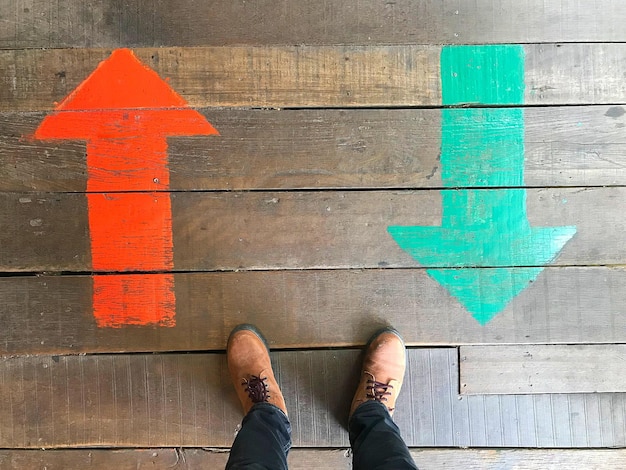 Photo low section of man standing by arrow symbols on wooden floor