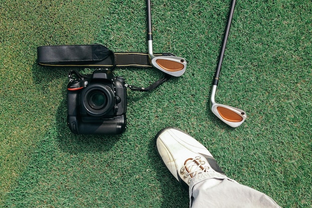 Foto sezione bassa dell'uomo in piedi dai club da golf e dalla telecamera sull'erba