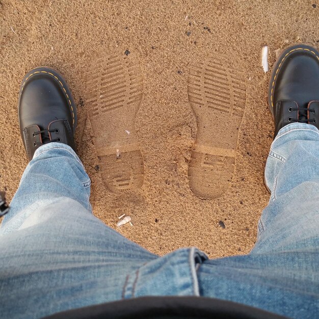 Foto sezione bassa di un uomo in piedi vicino alle impronte di scarpe sulla spiaggia