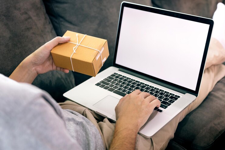 Photo low section of man using blank laptop while holding cardboard box on sofa at home