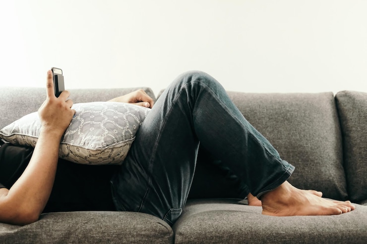 Photo low section of man using mobile phone while lying on sofa at home