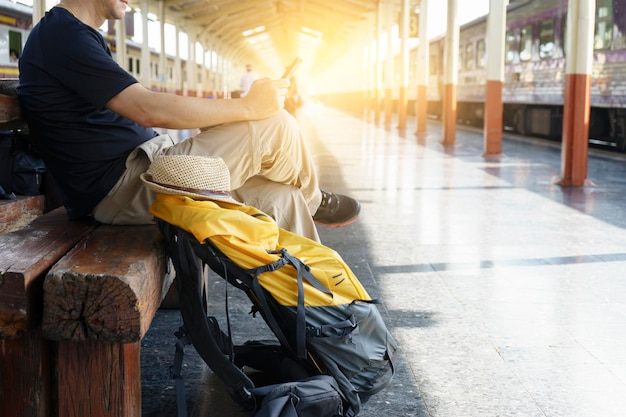 Foto sezione bassa dell'uomo che usa il telefono cellulare mentre è seduto sulla ferrovia alla piattaforma della stazione