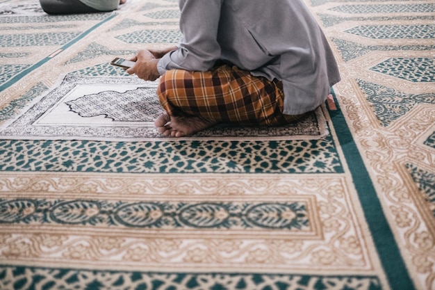 Low section of man using phone while sitting on carpet