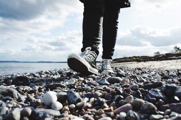 Low section of man walking at beach against sky