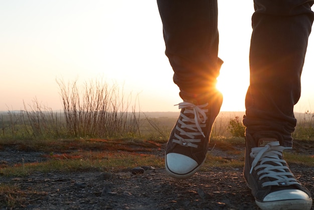 Low section of man walking on land against sky during sunset