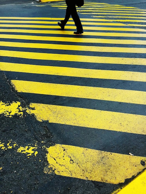 Foto sezione bassa di un uomo che cammina sul passaggio della zebra gialla