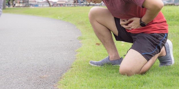 Foto sezione bassa di un uomo con mal di stomaco sull'erba lungo un sentiero nel parco