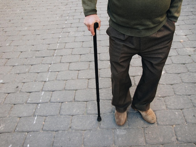 Foto sezione bassa di un uomo con un bastone da passeggio in piedi per strada