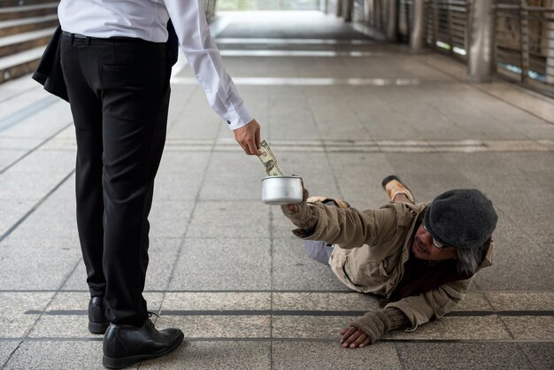 写真 乞食が持っている鉢に紙幣を入れるビジネスマンの下層階級