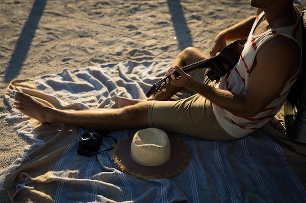 Фото Низкая часть кавказца, сидящего на пляже у моря и играющего на гитаре. здоровый отдых на свежем воздухе у моря.