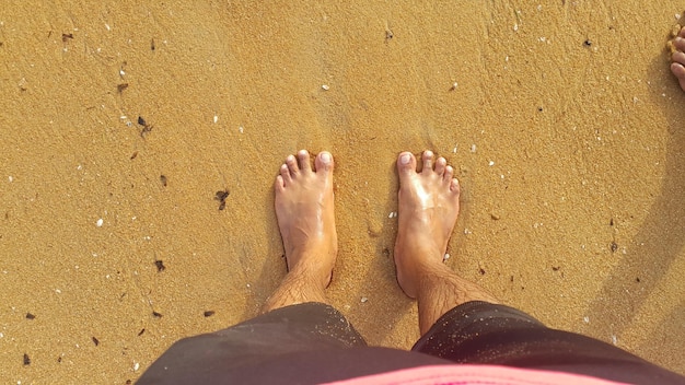 Фото Нижняя часть человека, стоящего на песчаном пляже.