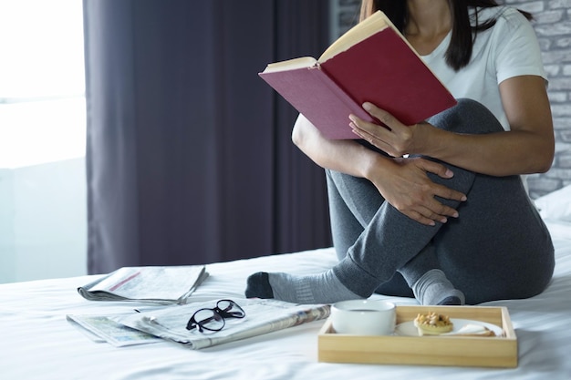 사진 집 에서 침대 에 아침 식사 를 하고 앉아서 책 을 읽는 젊은 여자 의 낮은 부분