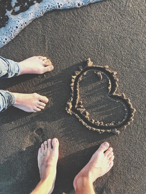 Photo low section of people standing by heart shape on sand at beach