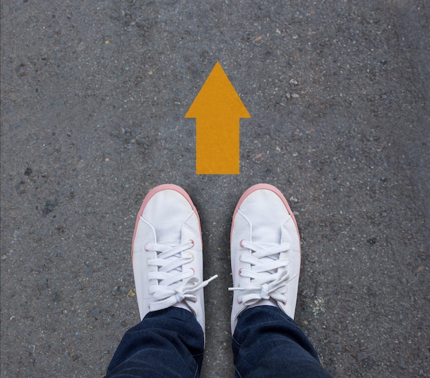 Photo low section of person by arrow symbol on road