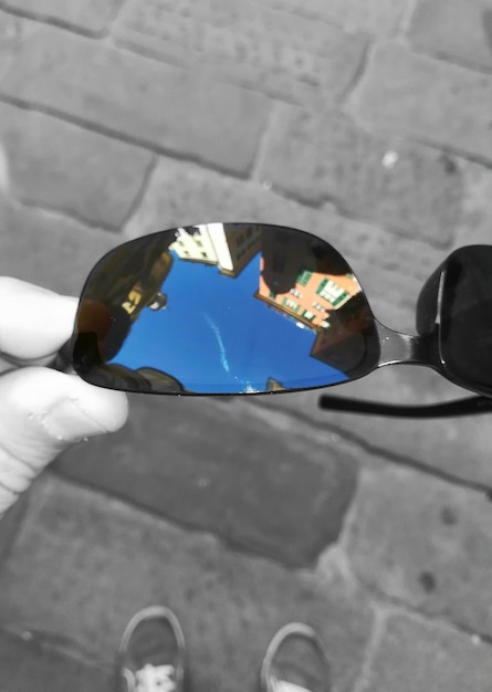 Low section of person holding sunglasses with reflection