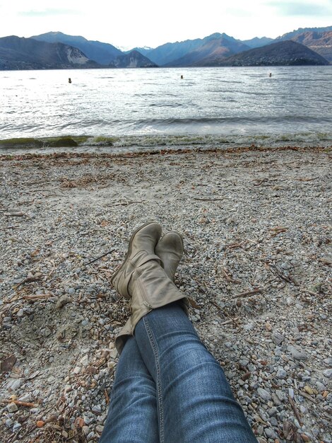 Photo low section of person resting on beach by mountains against clear sky